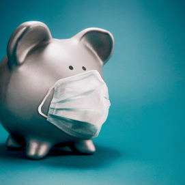 Close up of piggy bank, wearing protective face mask, isolated on blue background. Money saving concept in time of coronavirus pandemic.